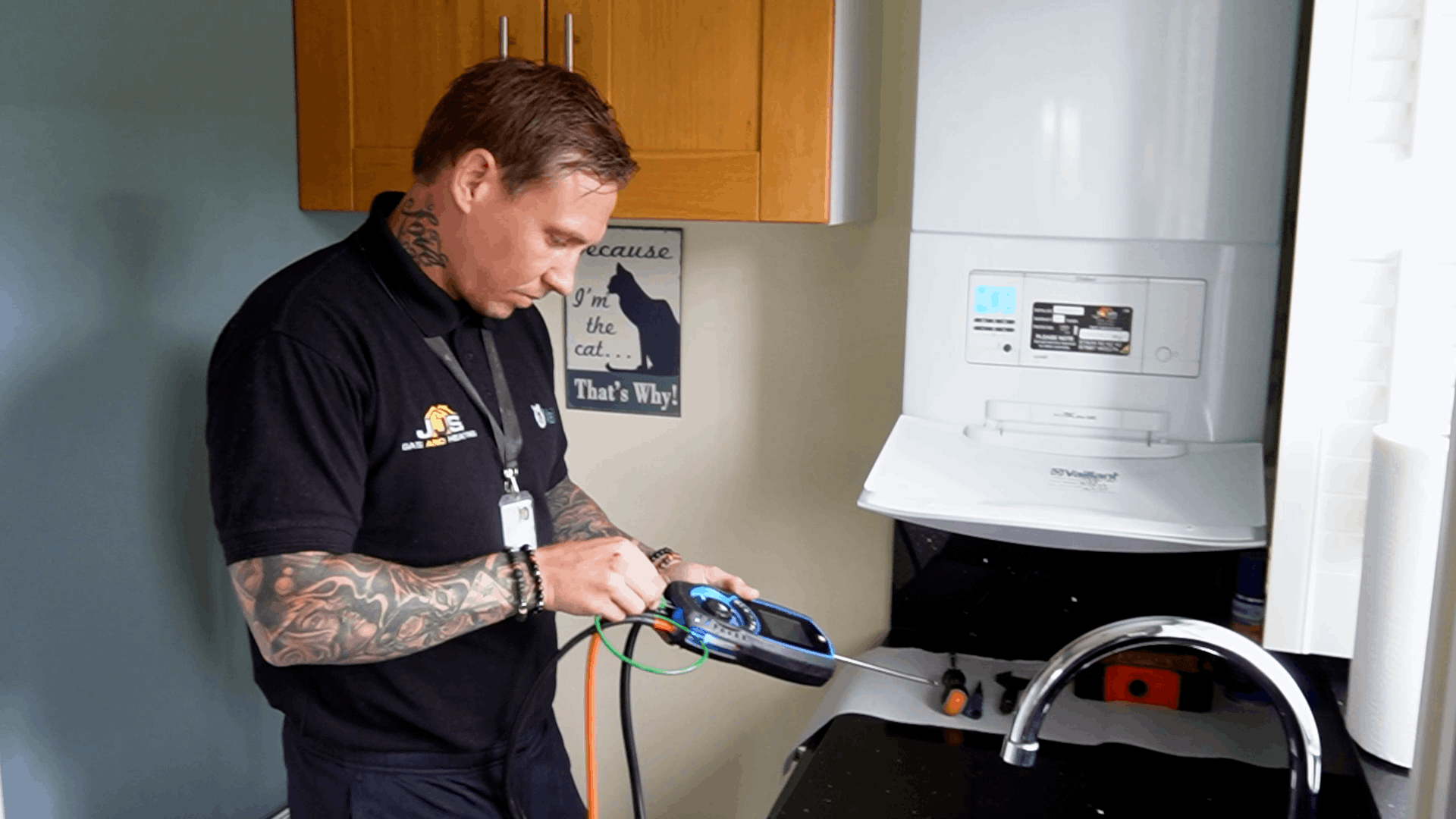 Technician with tattoos testing a device using a multimeter in a laundry room near a washer and sink.